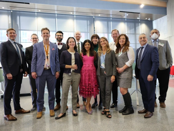 A group of people pose for a photo. They are wearing suits, ties, and dresses and are in a university building.