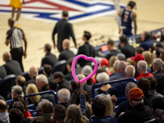 Fan holding up a pink balloon in the shape of a heart during basketball game
