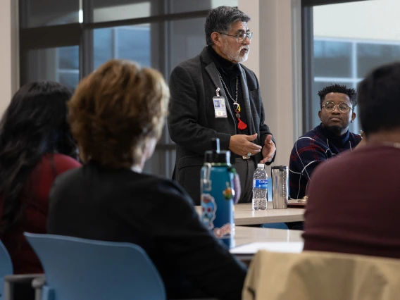 Person standing talks to a group sitting at a rectangular table.