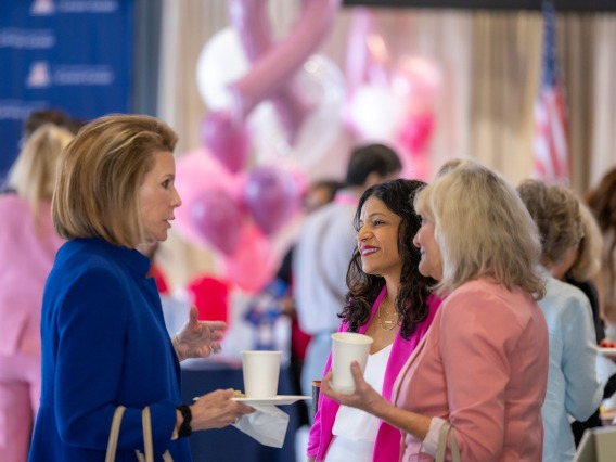 Three people, Dr. Rachna Shroff, Ginny L. Clements and Nancy Brinker talk together in the auditorium of the GLC Breast Cancer Research 2nd annual symposium
