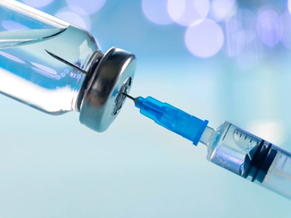 Closeup photo of a needle being injected into a syringe with blue background.