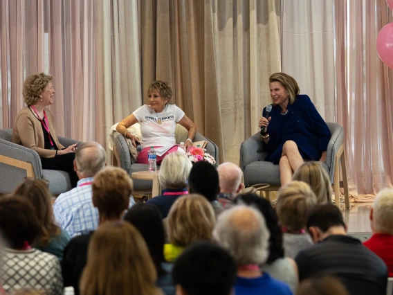 Three people sit around a table in front of an audience during the GLC Breast Cancer Research Symposium 