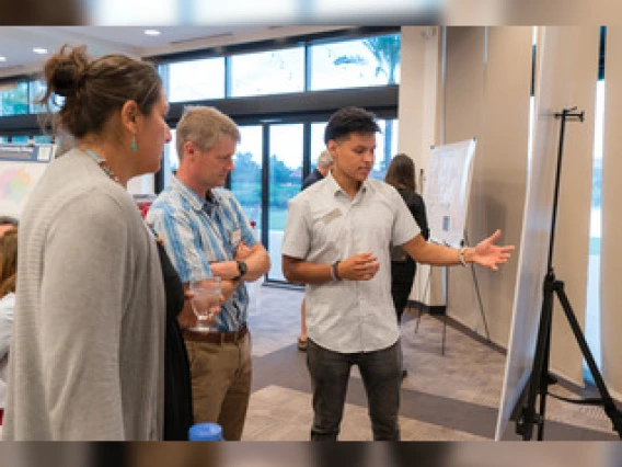 Three people are standing and examining a research poster on an easel.