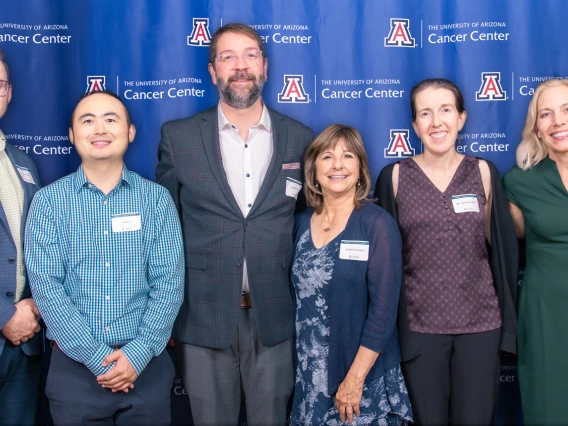 Eight Cancer Center award winners take a photo in front of a backdrop at an awards dinner.