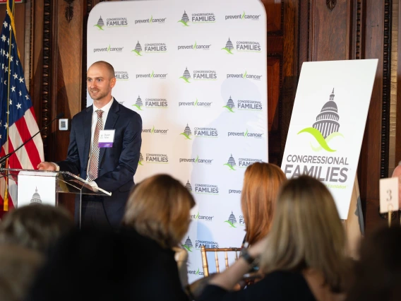 Person speaks at podium indoors in front of an audience. 