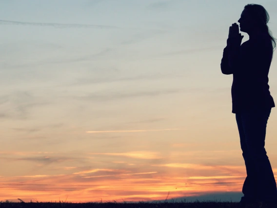 Silhouette of person meditating in front of a sunset.