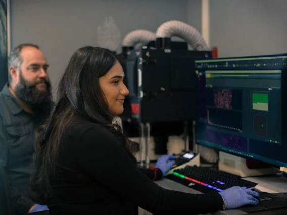 A student works on a computer in a lab at the cancer center with her mentor.