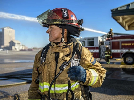 A female firefighters looks into the distance wearing full firefighting gear.