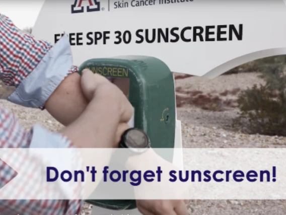 Person applying sunscreen in front of a University of Arizona sunscreen kiosk.