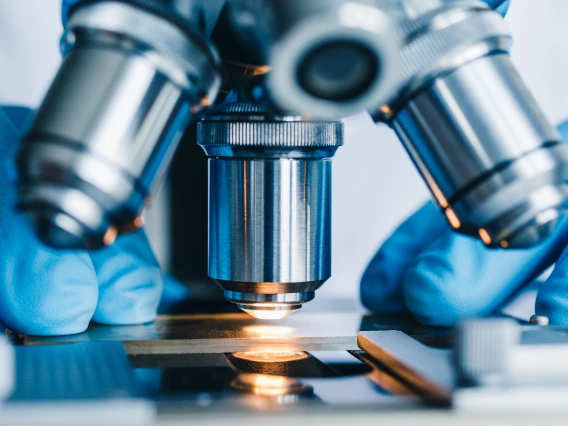 Microscope with slide and hands with blue medical gloves.