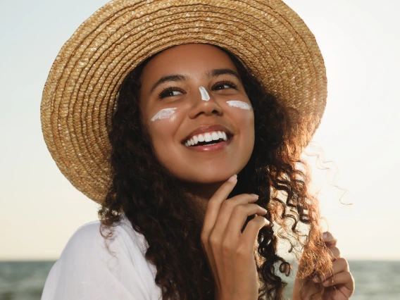 Person applying sunscreen and wearing a hat.