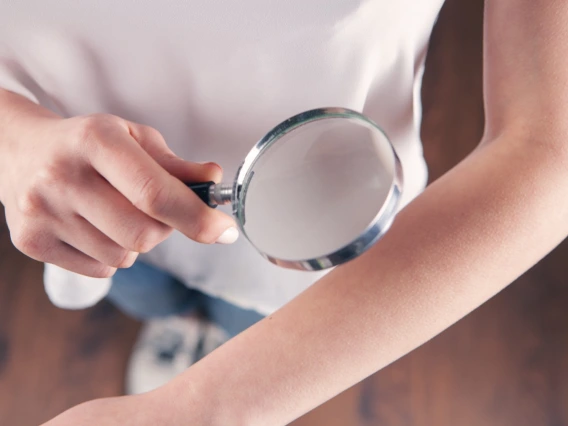 Person examining their own skin with a magnifying glass