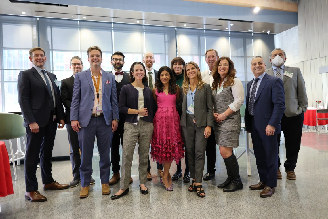 A group of people pose for a photo. They are wearing suits, ties, and dresses and are in a university building.