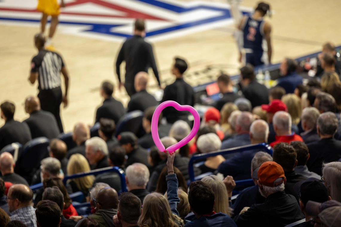 Fan holding up a pink balloon in the shape of a heart during basketball game