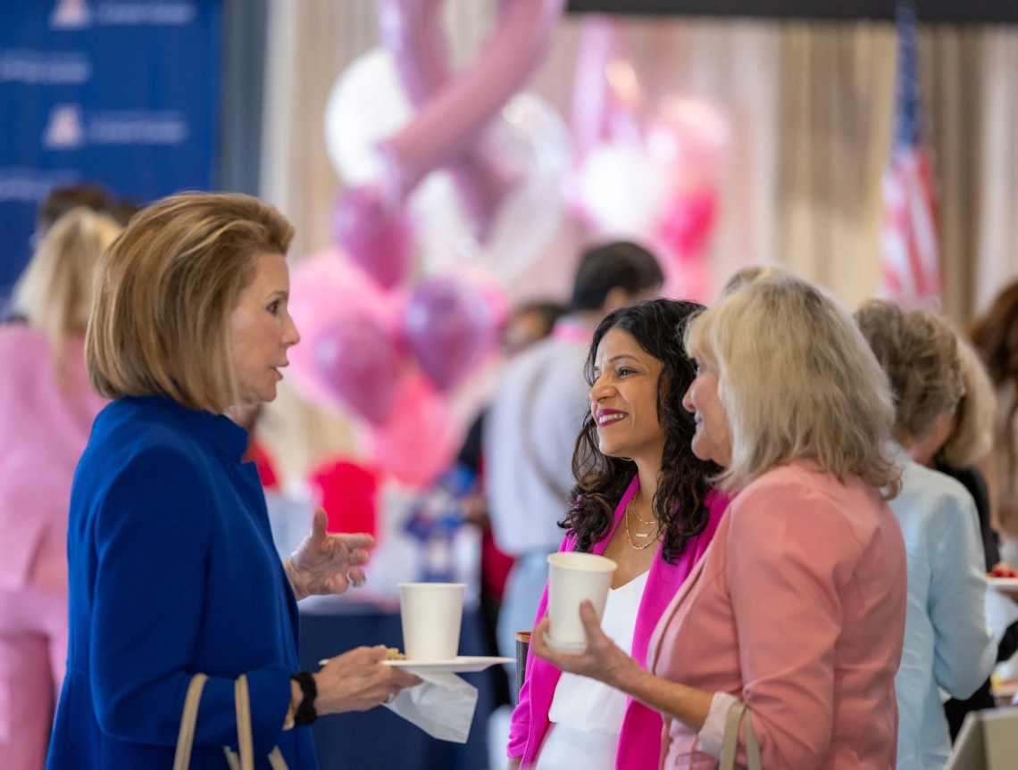 Three people, Dr. Rachna Shroff, Ginny L. Clements and Nancy Brinker talk together in the auditorium of the GLC Breast Cancer Research 2nd annual symposium