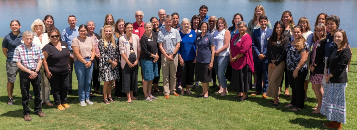 The NACP group poses for a photo on a lawn in front of a pond.