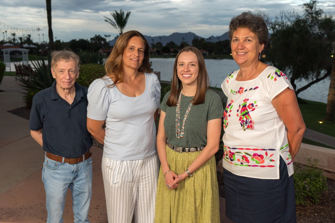 Four people pose for a photo standing outdoors at twilight.