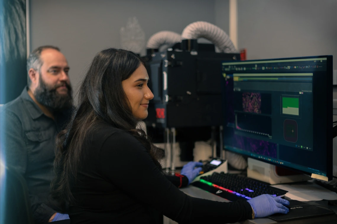 A student works on a computer in a lab at the cancer center with her mentor.