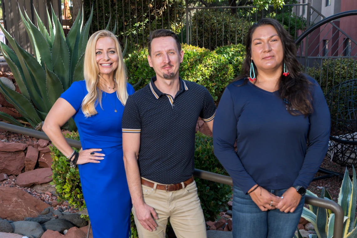 Three people stand for a group photo outdoors.