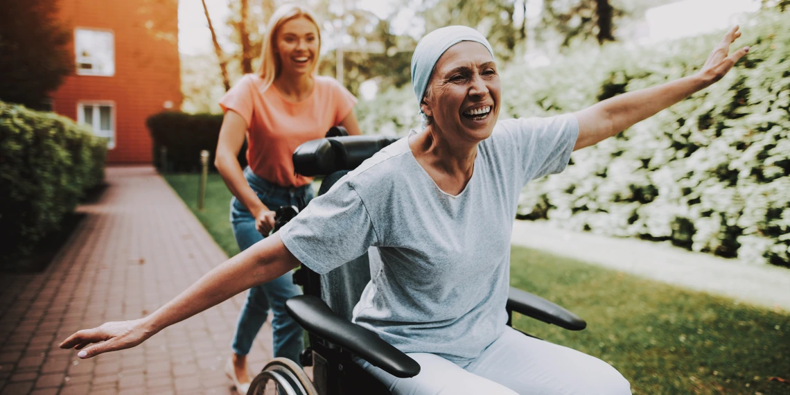 Person in wheelchair wearing a head scarf with arms extended pushed by their daughter 