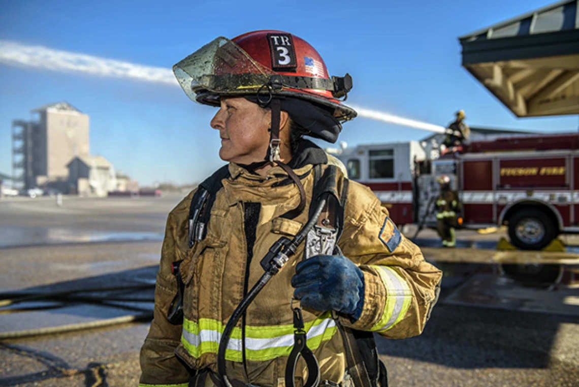 A female firefighters looks into the distance wearing full firefighting gear.