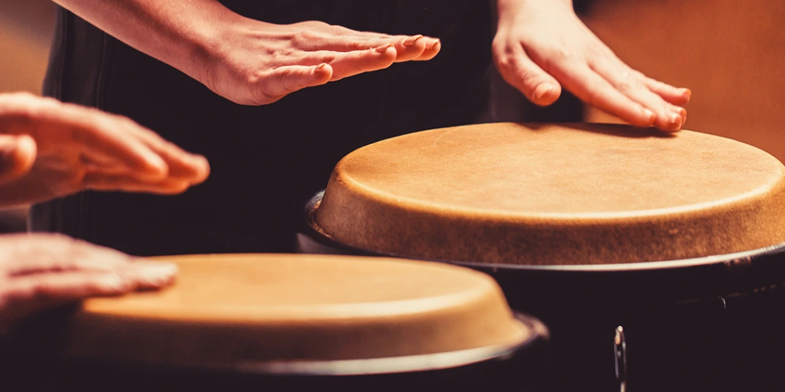 Two people play drums with their hands.