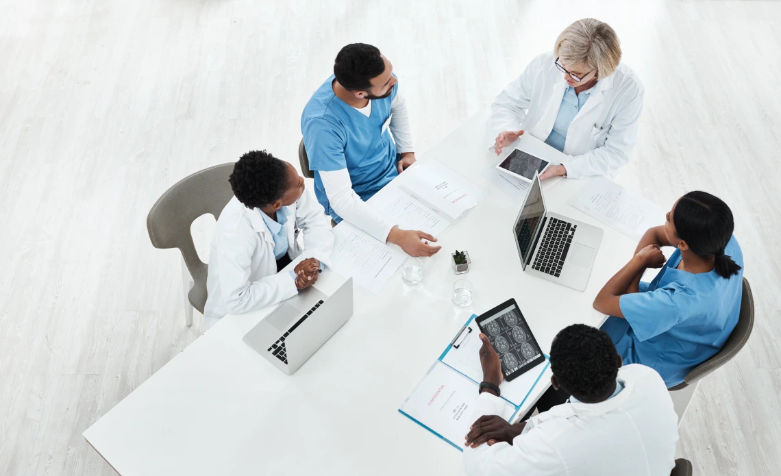 Healthcare workers sit around a white rectangular table.