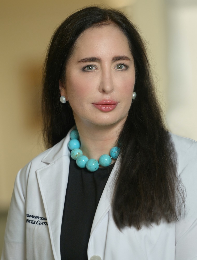 Person wearing a white lab coat and a turquoise necklace. She has long, straight dark hair.