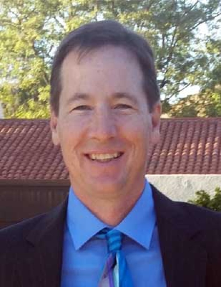 Person with a blue button-down shirt and blue striped tie with a black jacket. He is smiling.