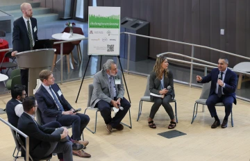 A group sits in chairs onstage in a semi-circle in front of a speaker at the podium.