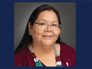 Person with long, straight dark hair and glasses smiles for a portrait. She has rectangular glasses, a maroon shirt and a beaded necklace.