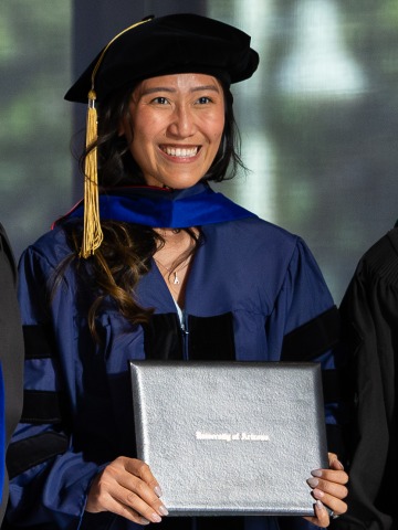 Person wearing a graduation cap and gown poses with their diploma.