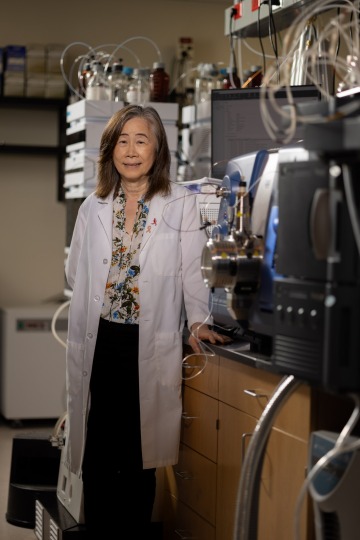 A portrait of Sherry Chow in a lab coat leaning against a counter in her lab.