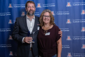 Dr. Andrew Paek and Dr. Joyce Schroeder pose for a photo during the Awards Dinner. They are standing in front of a backdrop, and Dr. Paekis holding an award.