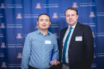 Dr. Jianqin Lu and Dr. Steffan Nawrocki pose for a photo during the Awards Dinner. They are standing in front of a backdrop, and Dr. Lu is holding an award.