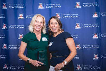 Dr. Heidi Hamann  and Dr. Gloria Coronado pose for a photo during the Awards Dinner. They are standing in front of a backdrop, and Dr. Hamann is holding an award.