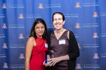 Dr. Jennifer Erdrich and Dr. Rachna Shroff pose for a photo during the Awards Dinner. They are standing in front of a backdrop, and Dr. Erdrich is holding an award.