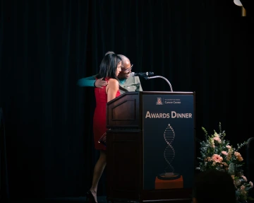 Rachna Shroff, MD, and Juanita Merchant, MD, hug at the podium while Dr. Merchant presents Dr. Shroff with her award.