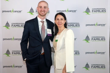 Two people pose for a photo in front of a backdrop.