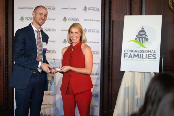 Two people pose in front of a backdrop holding a glass award.