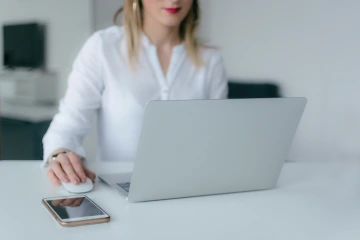 Person uses a mouse sitting at a table in front of a laptop.