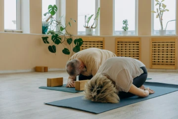 Two people sit in child's pose on separate yoga mats in a yoga studio