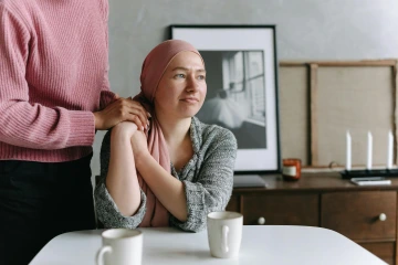 woman wearing head scarf sitting at table holding a friend's hand