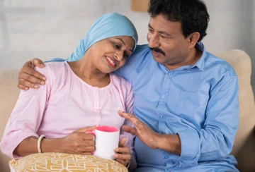 Person hugs another person who is sick and holding a mug. 