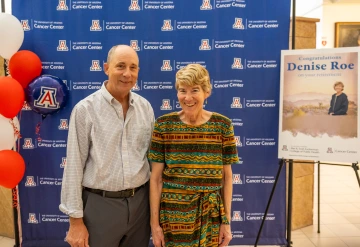 Ron Lynch and Denise Roe pose for a photo standing in front of a U of A Cancer Center backdrop at Roe's retirement party.