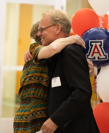 Denise Roe hugs Georg Wondrak at her retirement party with balloons in the background.