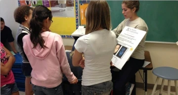 Students learn about sun safety from a person holding a poster.