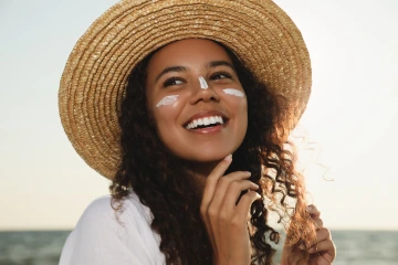 Person applying sunscreen and wearing a hat.