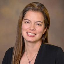 A person smiles with long brown hair. She is wearing a black shirt.