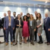 A group of people pose for a photo. They are wearing suits, ties, and dresses and are in a university building.